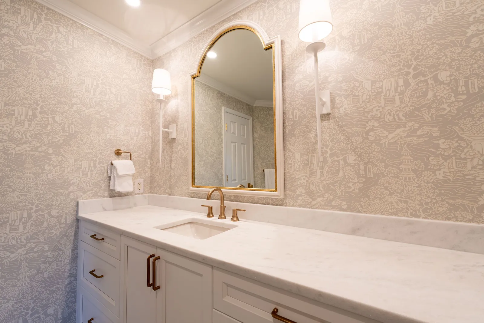 Vanity with a white quartz counter, brass faucet and a tall brass-framed arched mirror