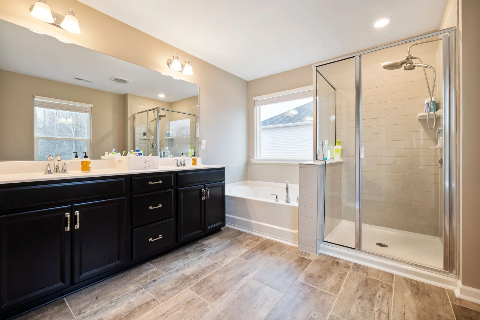 Primary bathroom with a long double vanity, a soaking tub under a window and a glass-enclosed shower