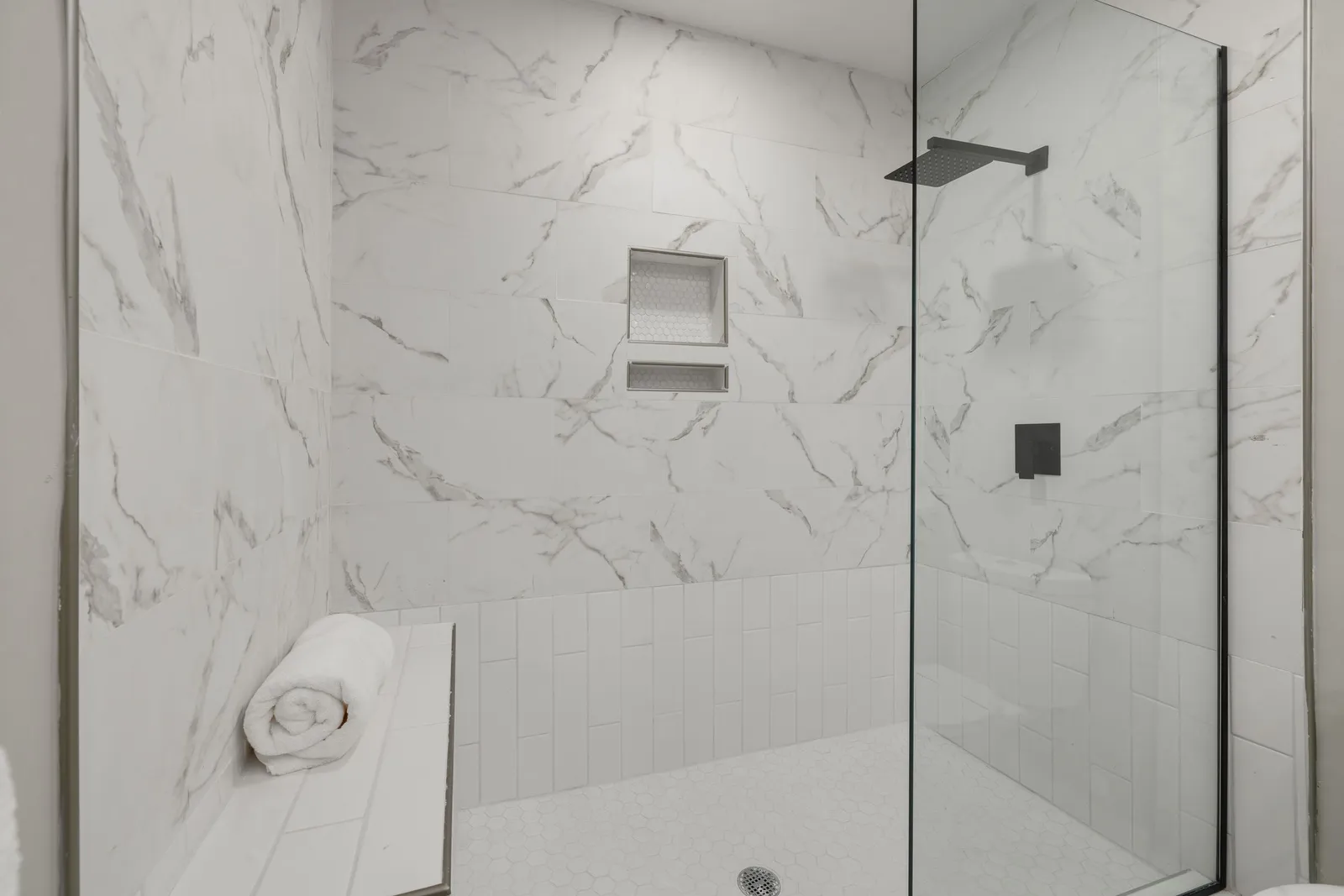 Walk-in shower with white marble-look tile, a built-in bench, a recessed niche and black fixtures